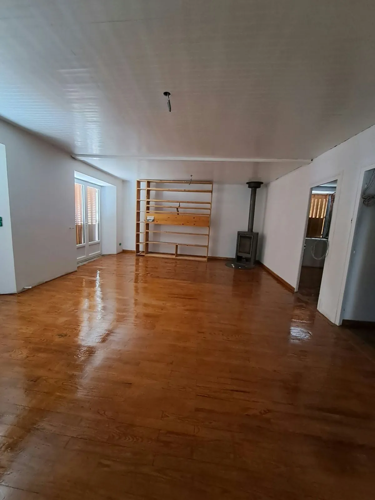 Grande pièce au parquet vitrifié, plafond en lambris blanc et poêle à bois